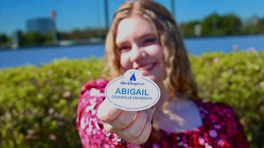 Abigail Foster standing beside a lake holding out her Disney name tag.