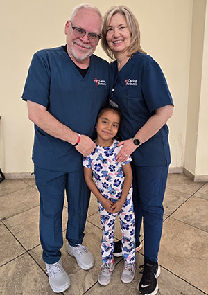 Two doctors stand with a young girl whose life they saved.