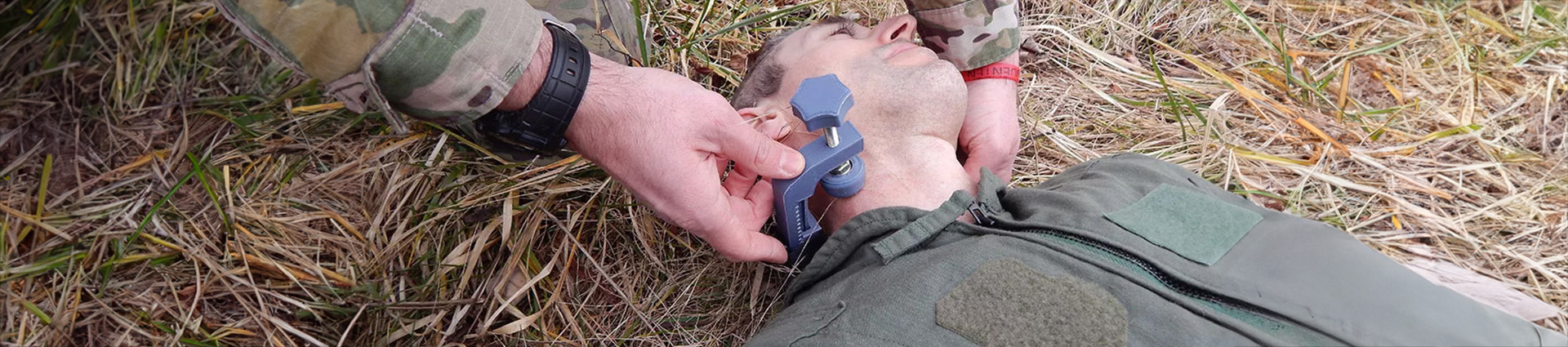 ARC Trauma clamp being demonstrated on a man lying on the ground in green military uniform.