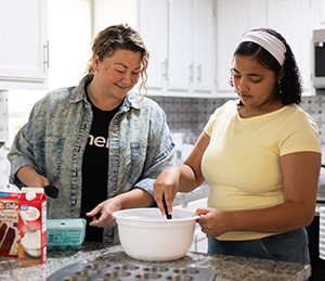 Two women mixing batter for a cake.