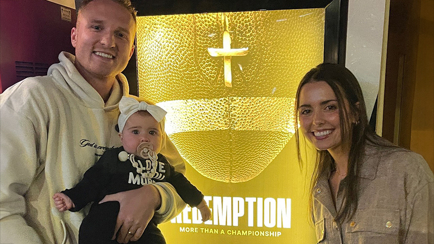 Matt and Marlee Benson with their daughter in front of a Redemption movie poster.