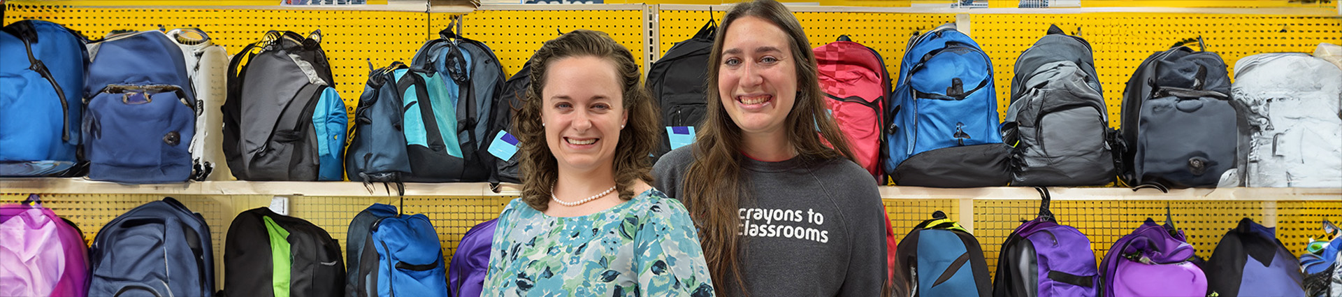 Dr. Megan Brown and Malena Ball standing in front of backpacks at Crayons to Classrooms.