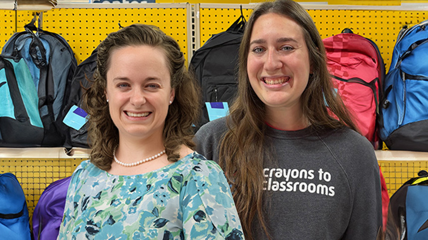 Dr. Megan Brown and Malena Ball standing in front of backpacks at Crayons to Classrooms.