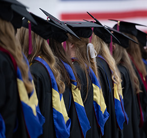 Students in caps and gowns with blue and gold hoods from behind.