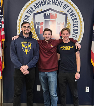 Three young men standing in front of the seal for Cedarville University's Center for the Advancement of Cybersecurity.