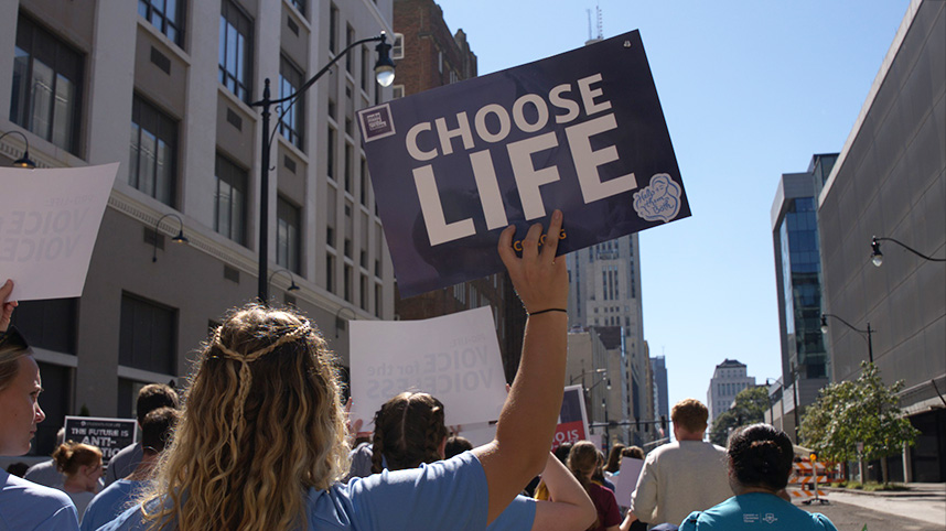 Woman marching on city street holding a sign that says choose life.