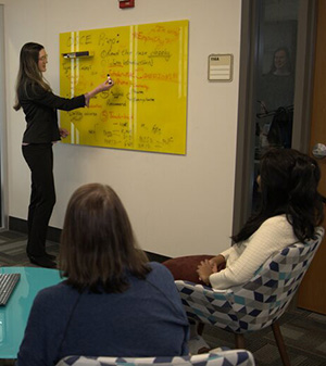 Dr. Kyrie Baden works at a white board as the research team looks on.