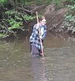 Abby Paulding standing in a creek collecting midges with a net.