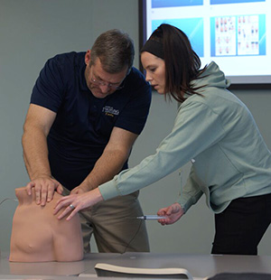 Nursing student practices giving a shot using a mannequin.