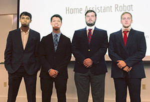 A senior design team of four young men in suits pose for a photograph.