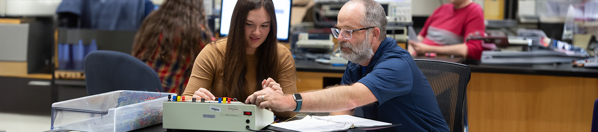 Male professor works with female student in electrical engineering lab.
