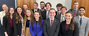 15 students pose for a photo at a speech and debate tournament.
