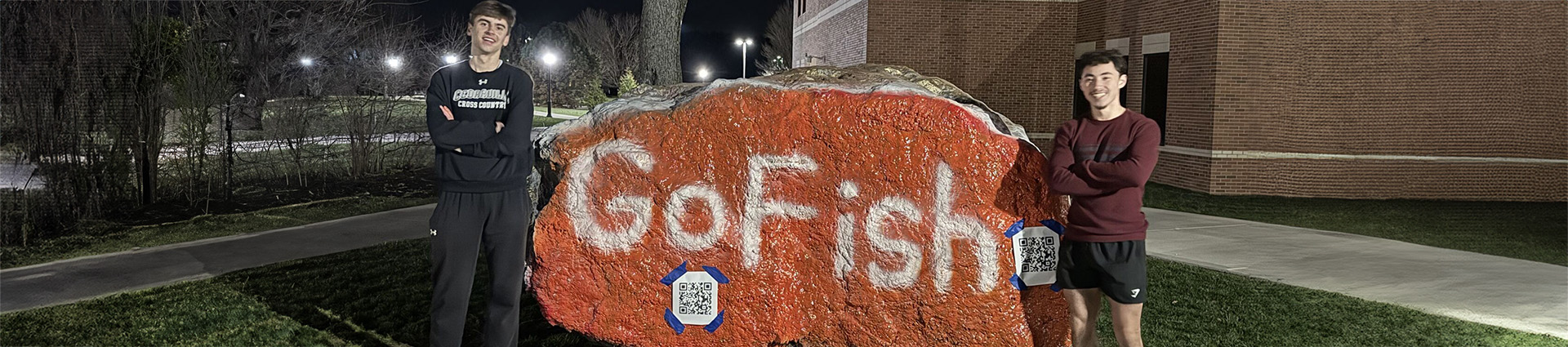 Andrew Bruckart and Jonathan Ellington stand beside "the rock" painted orange with the words "Go Fish."