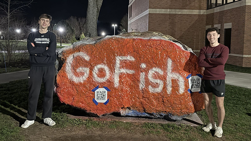 Andrew Bruckart and Jonathan Ellington stand beside "the rock" painted orange with the words "Go Fish."