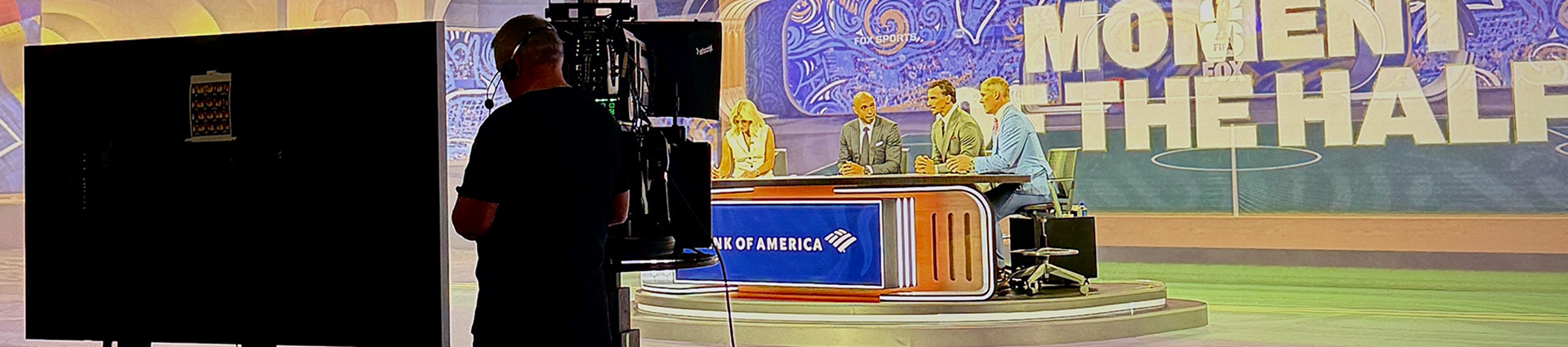 The news desk and personalities from behind a camara man in the FOX Sports studio.