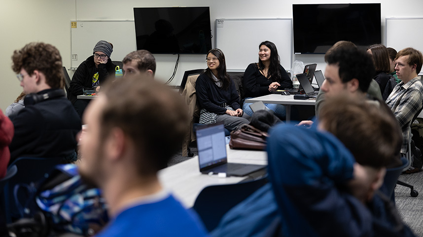 Several students seated at computers smile as they receive instructions.