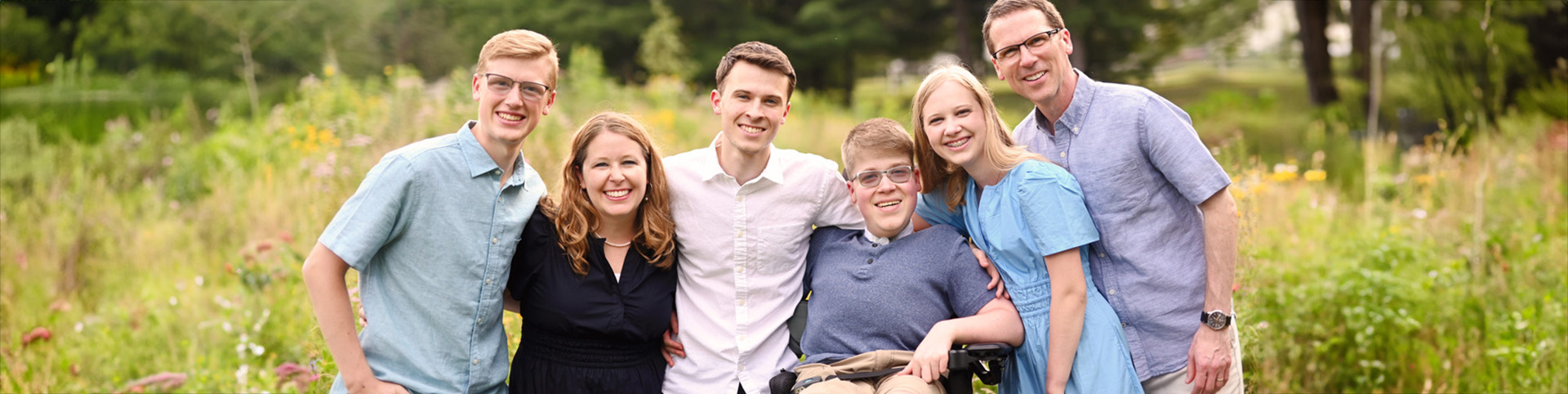 Carrie Holt, her husband, three sons and daughter pose for an outdoor family photo in a field of flowers.