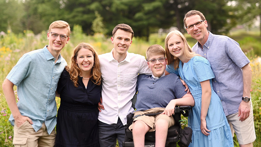 Carrie Holt, her husband, three sons and daughter pose for an outdoor family photo in a field of flowers.