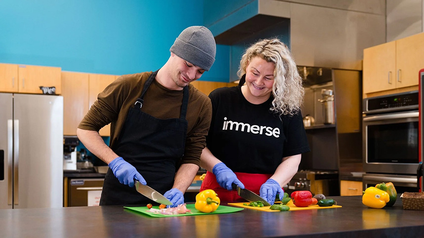 A volunteer at Immerse Arkansas works with a young man while preparing a meal.