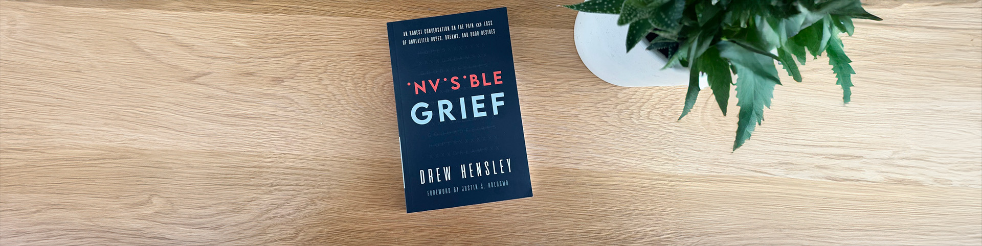 Invisible Grief book on a table beside a plant.