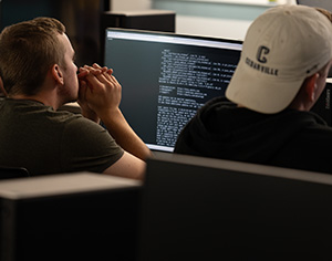 Student at Computer beside student wearing a Cedarville University ball cap.