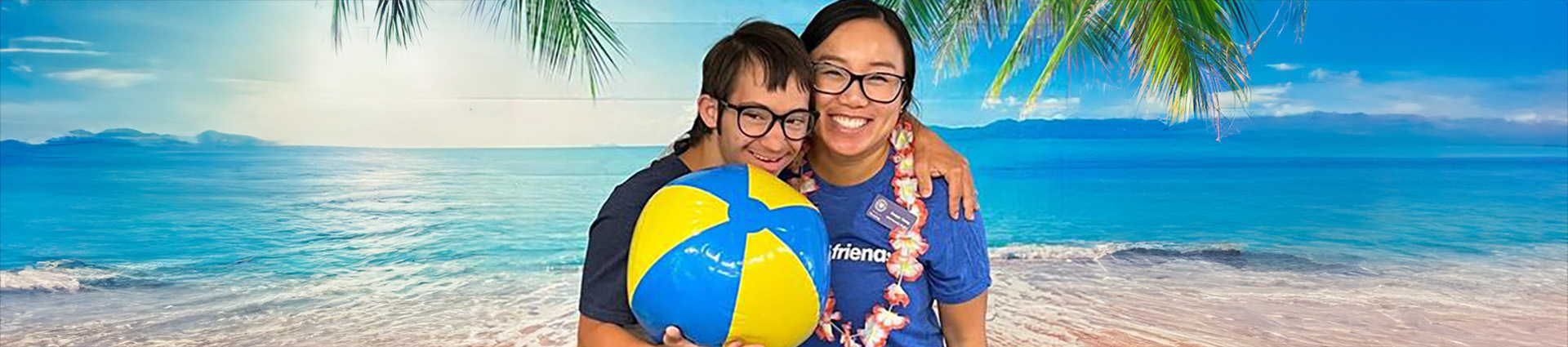 A Joni and Friends volunteer poses with a young man for a picture in front of a beach scene.