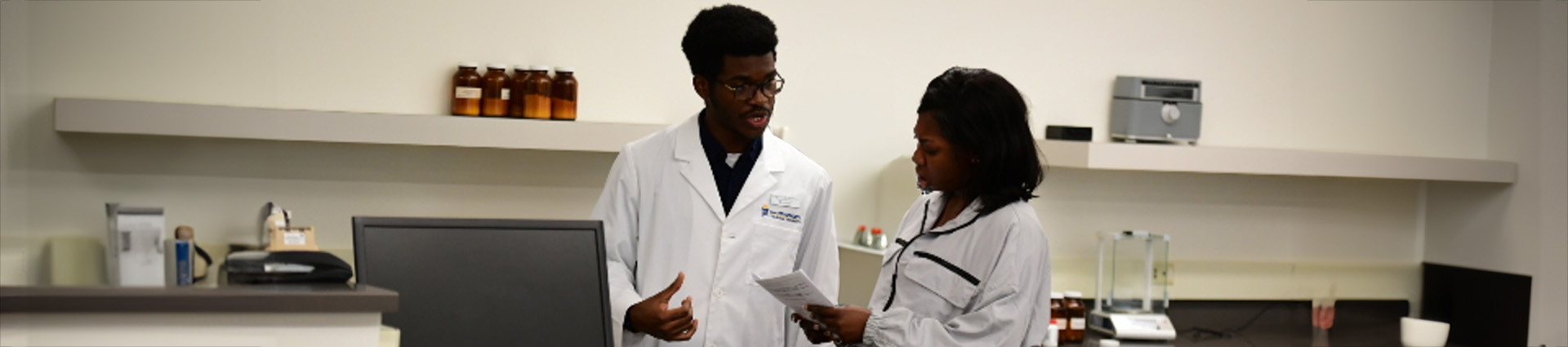 Chukwunonso Chukwuemeka speaks with Jane Addai in pharmacy lab.