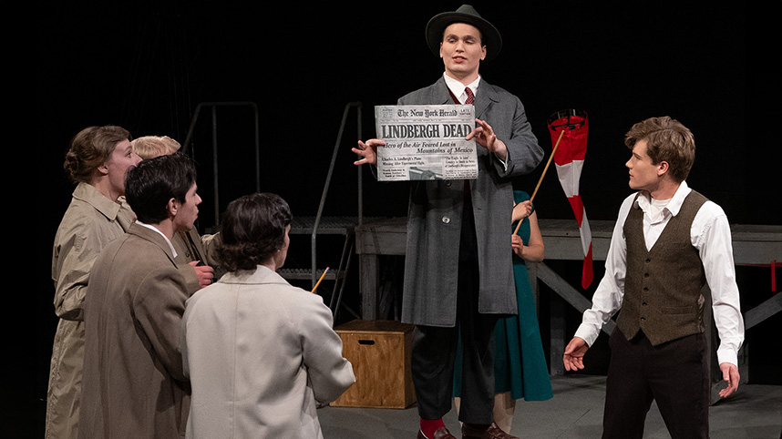 Students dressed as 1920s reporters surround an actor protraying the young Charles Lindbergh.