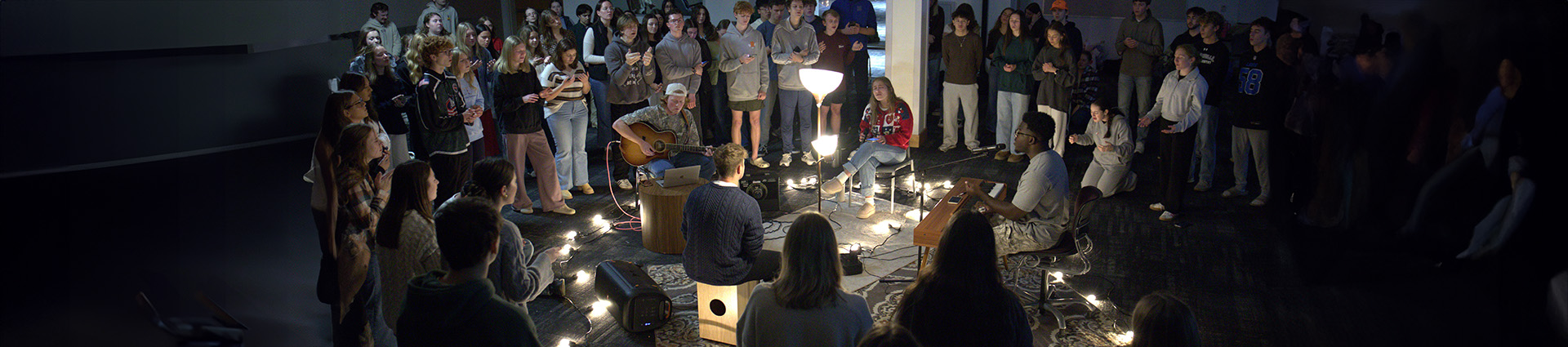 Students gather in a room lit only by lamps to focus on worship without distraction.
