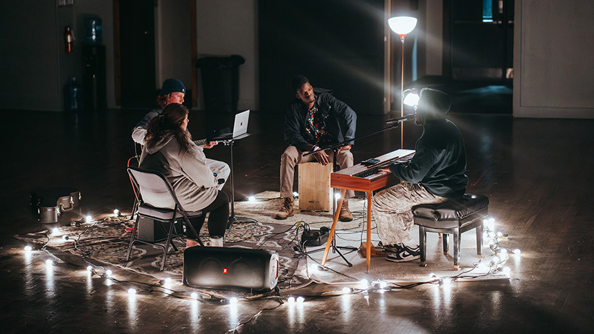 A small team of musicians play in a pool of lamplight.
