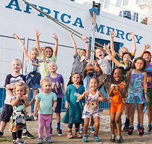 Children cheering on the dock beside a Mercy Ship.