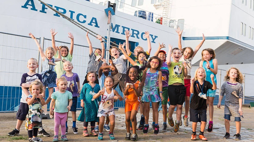 Children cheering on the dock beside a Mercy Ship.