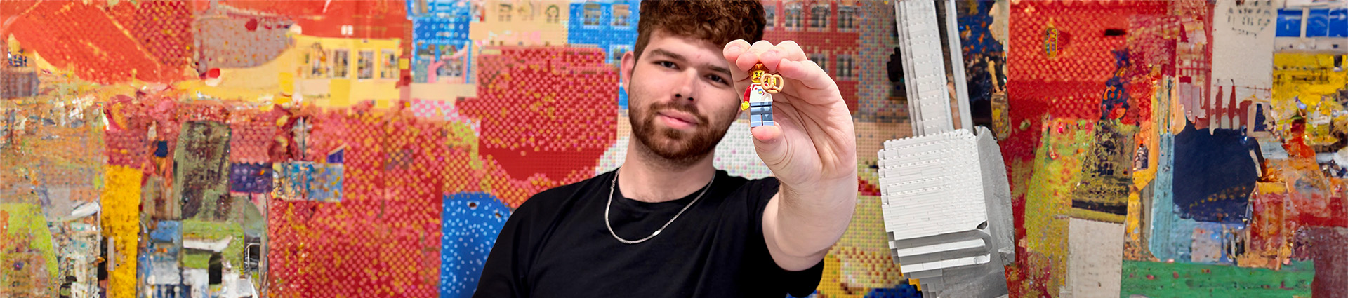 Micah Torres holds a LEGO minifigure while standing in front of a wall of LEGO images.