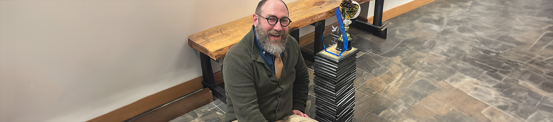 Professor Eric Mishne sits beside a stack of awards won by Cedarville University's forensics team.