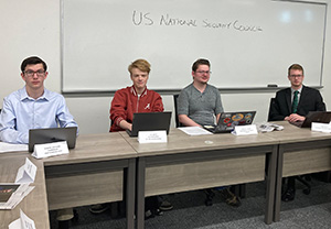 Four young men sitting at desks during a mock security council classroom exercise.