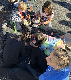 Elementary-aged students at the Ark of H.O.P.E. and a Cedarville student play with paints outside.