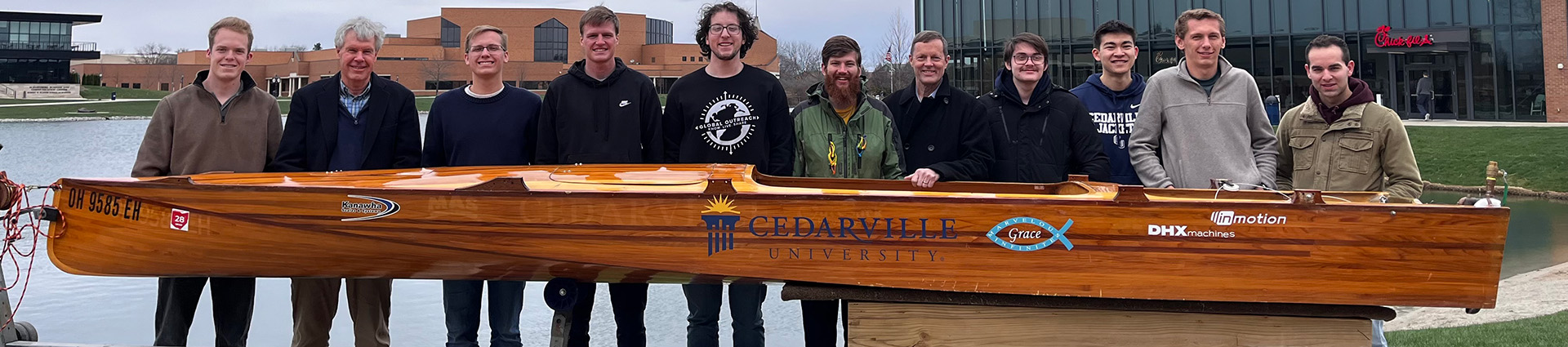 Engineering students stand beside the wooden electric boat they will race in the PEP competition.