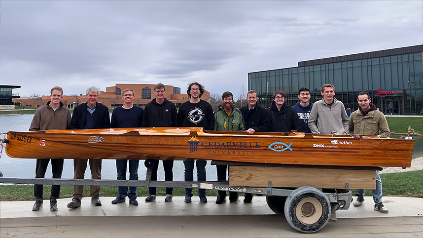 Engineering students stand beside the wooden electric boat they will race in the PEP competition.