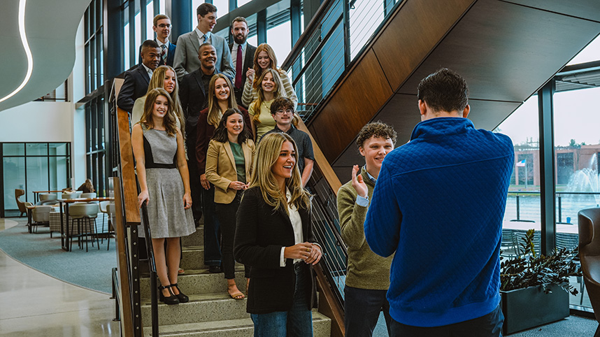 A group of students stand on a staircase as another takes their photograph.