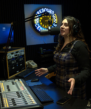 Female students speaks into a microphone in the Resound Radio studio.