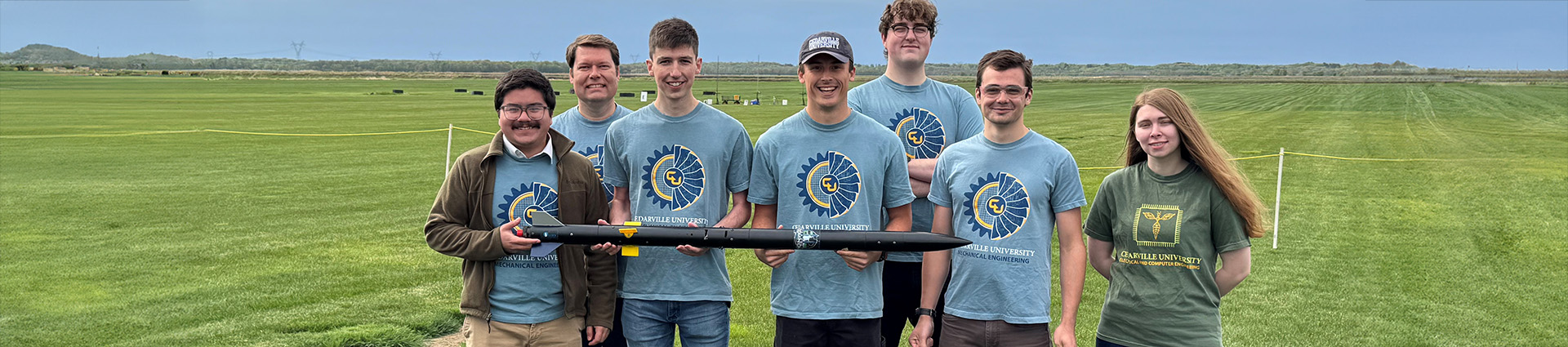 Rocketry team poses with their rocket on a green Minnesota field.