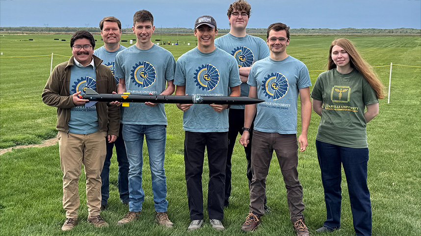 Rocketry team poses with their rocket on a green Minnesota field.