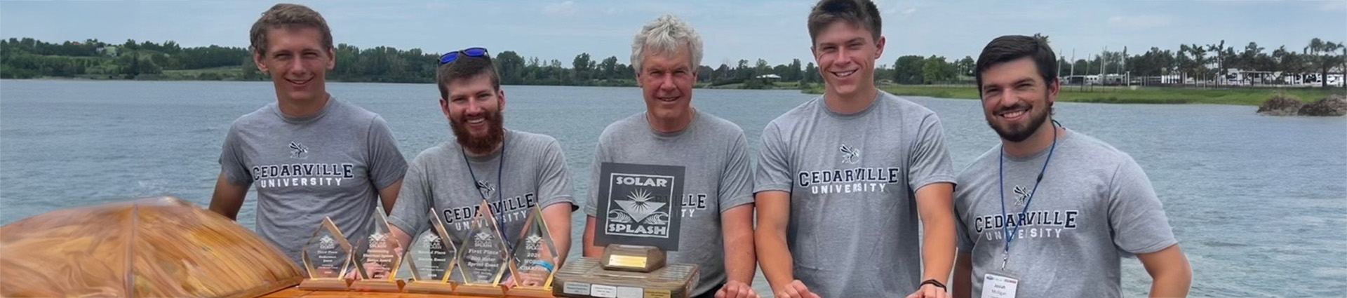 Solar Splash team of 4 students and Dr. Dewhurst with trophies sitting on the boat.