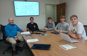 Four young men and a professor sit around a table.