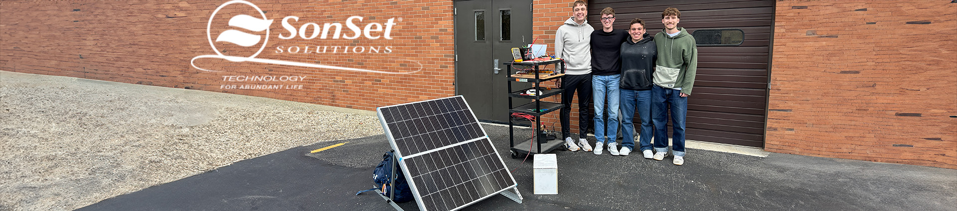 Four young men stand near the solar controller they built for SonSet Solutions for use on the mission field.