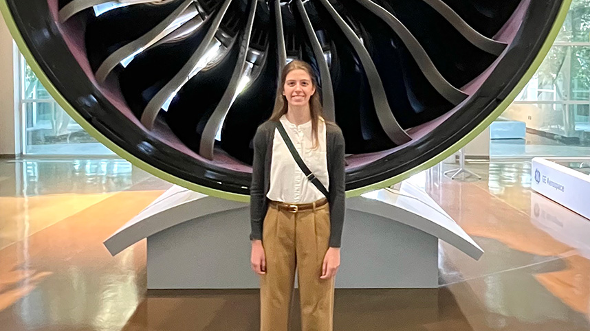 Madelyn Torrans stands in front of a jet engine and GE Aerospace.