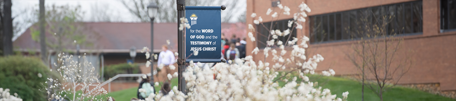 Lamp post banner that says "For the Word of God and the testimony of Jesus Christ" with spring flowers in the foreground.