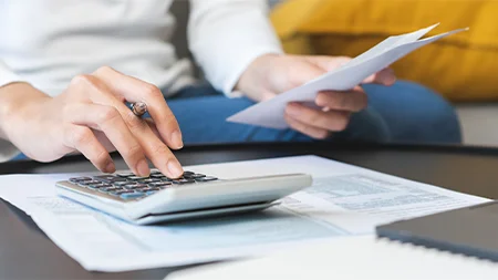 Person using a calculator while reviewing financial documents and education costs.