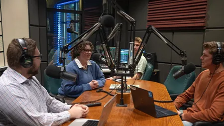 Cedarville University students record a podcast in campus radio studio with microphones and laptop.