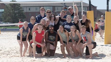 Group of students smiling on sand volleyball court